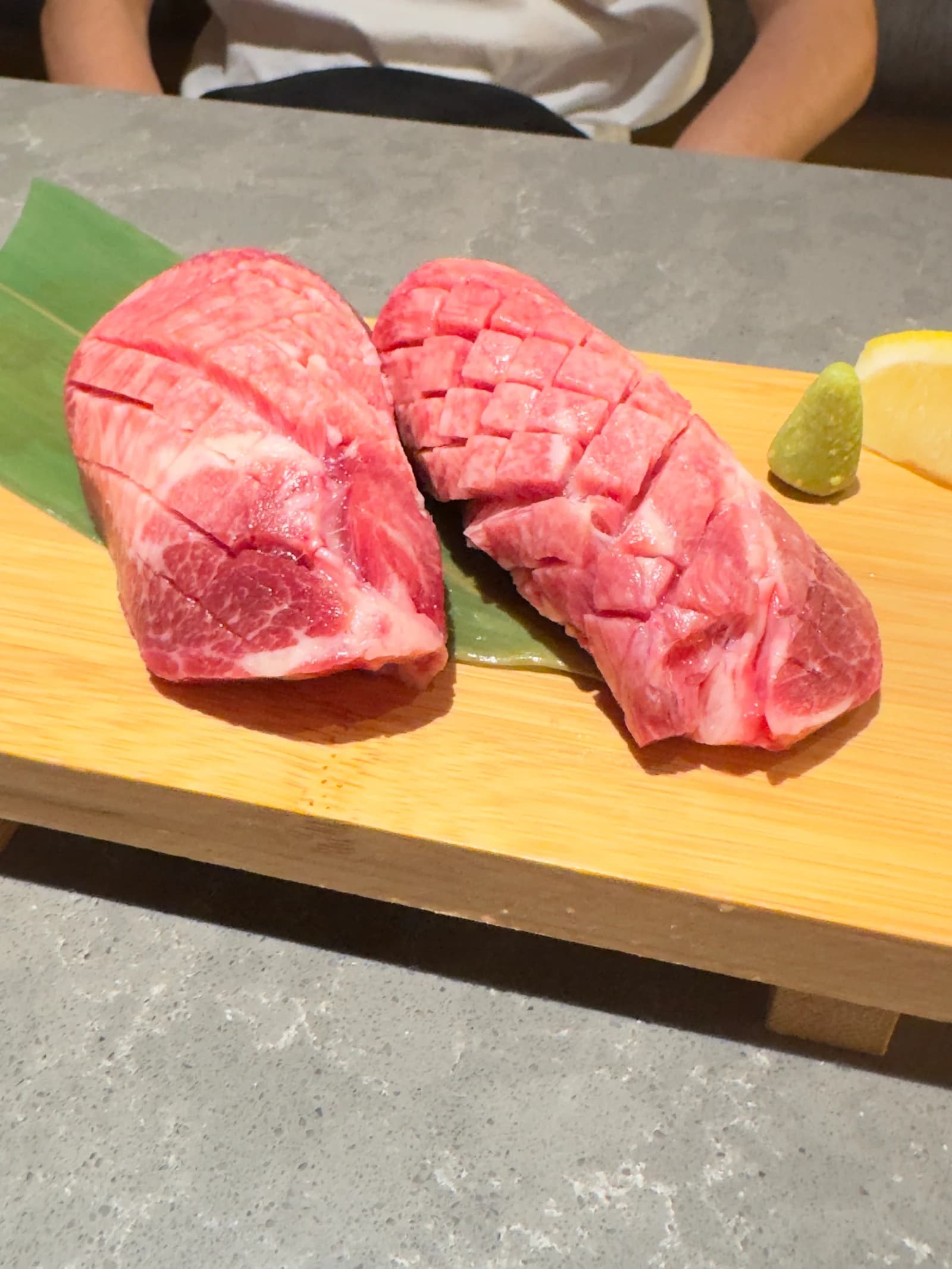 Two pieces of marbled beef on a wooden tray with lemon and wasabi at Gyu-Kaku