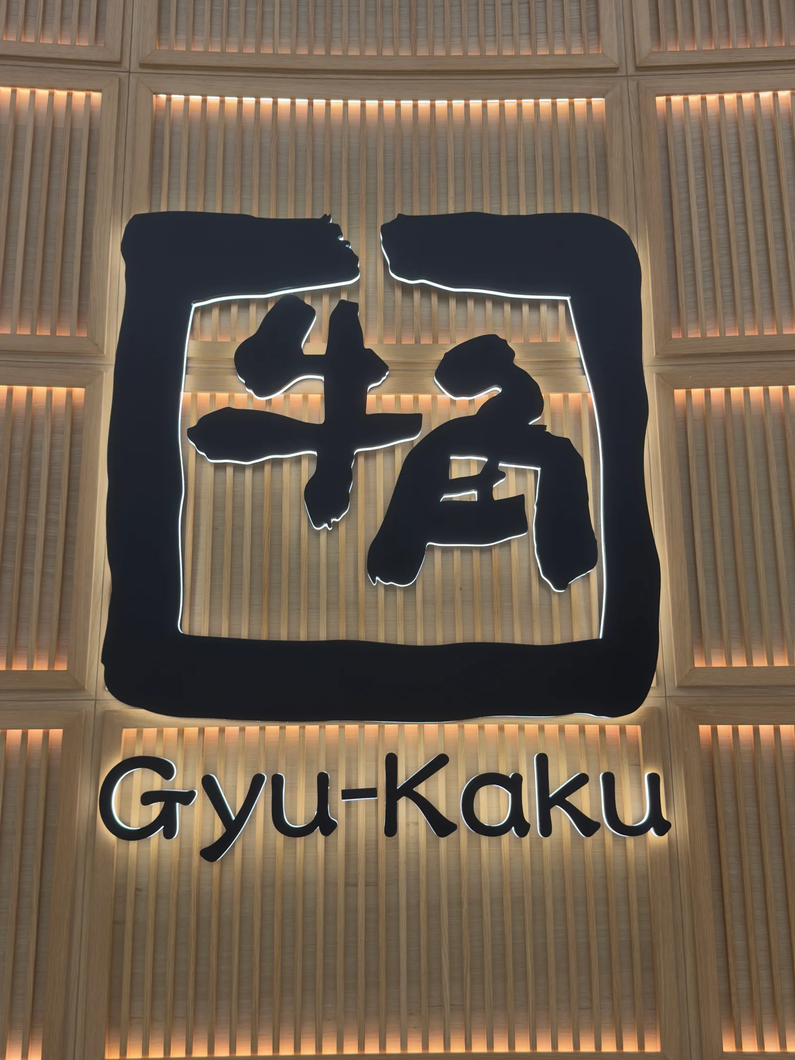 Gyu-Kaku Japanese BBQ logo in Japanese and English on a wooden slat wall