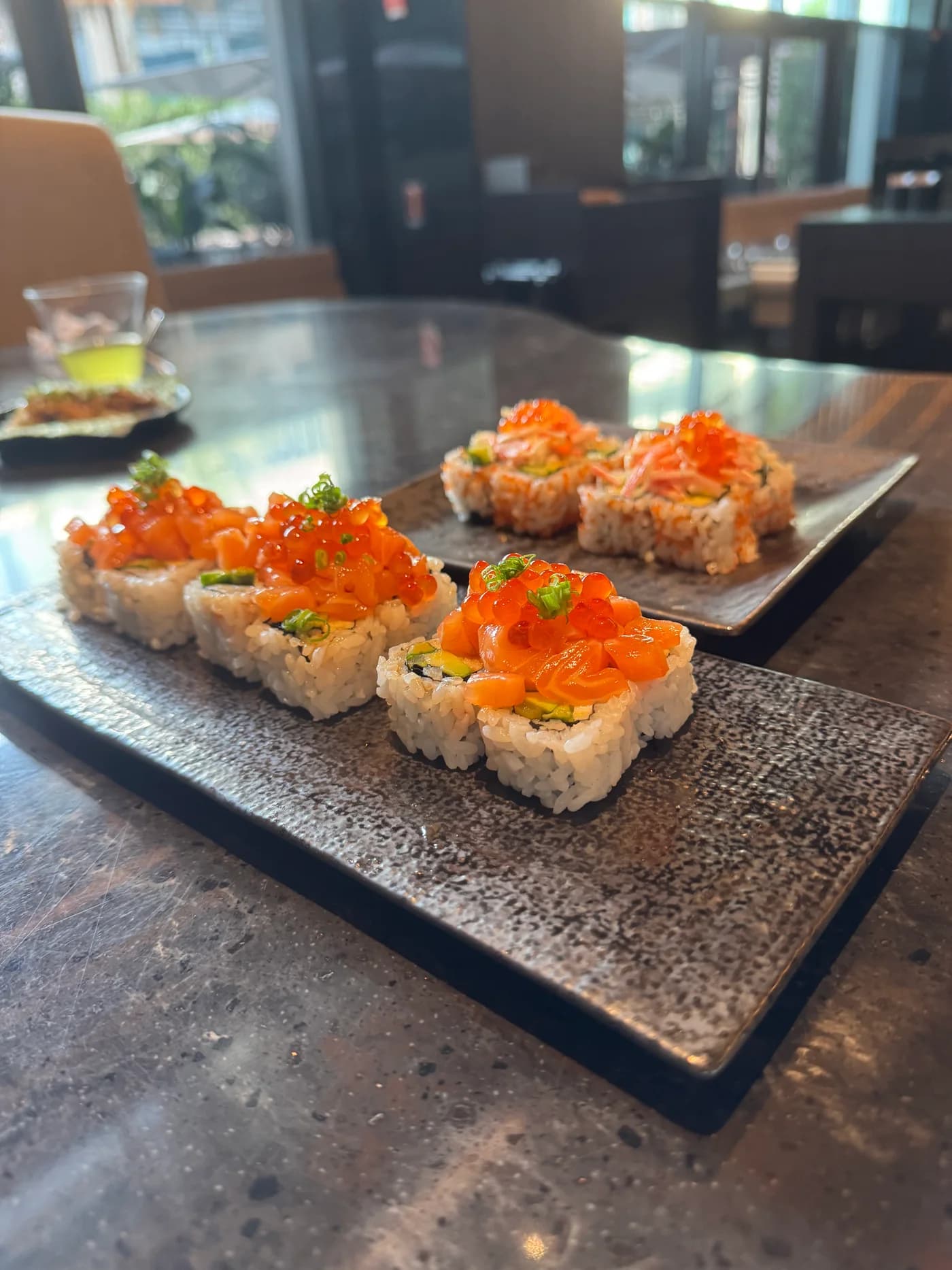 Sushi rolls with orange fish and roe toppings on dark plates at Kasumigaseki