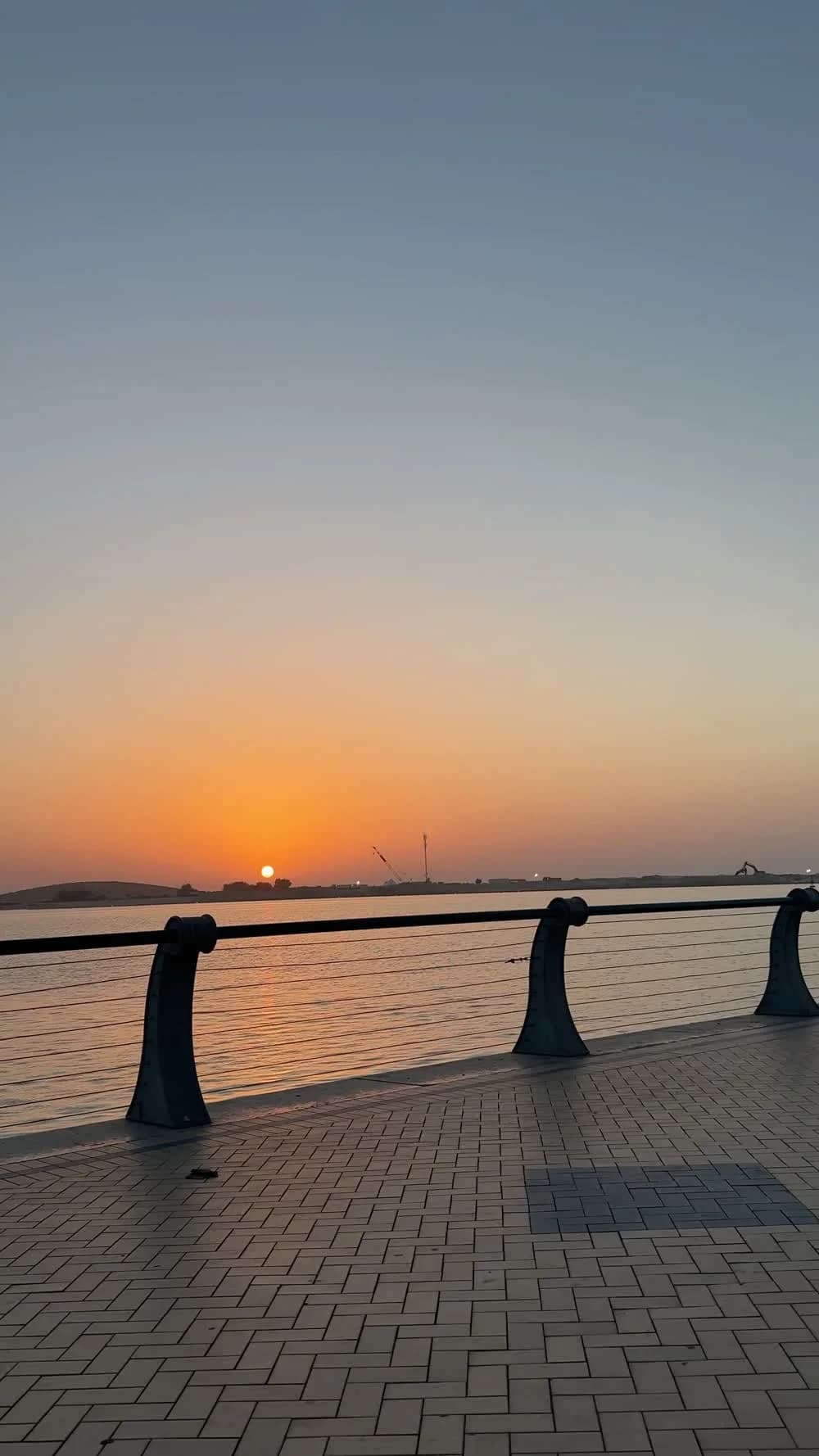 An orange sunset over the water beside a paved Abu Dhabi promenade